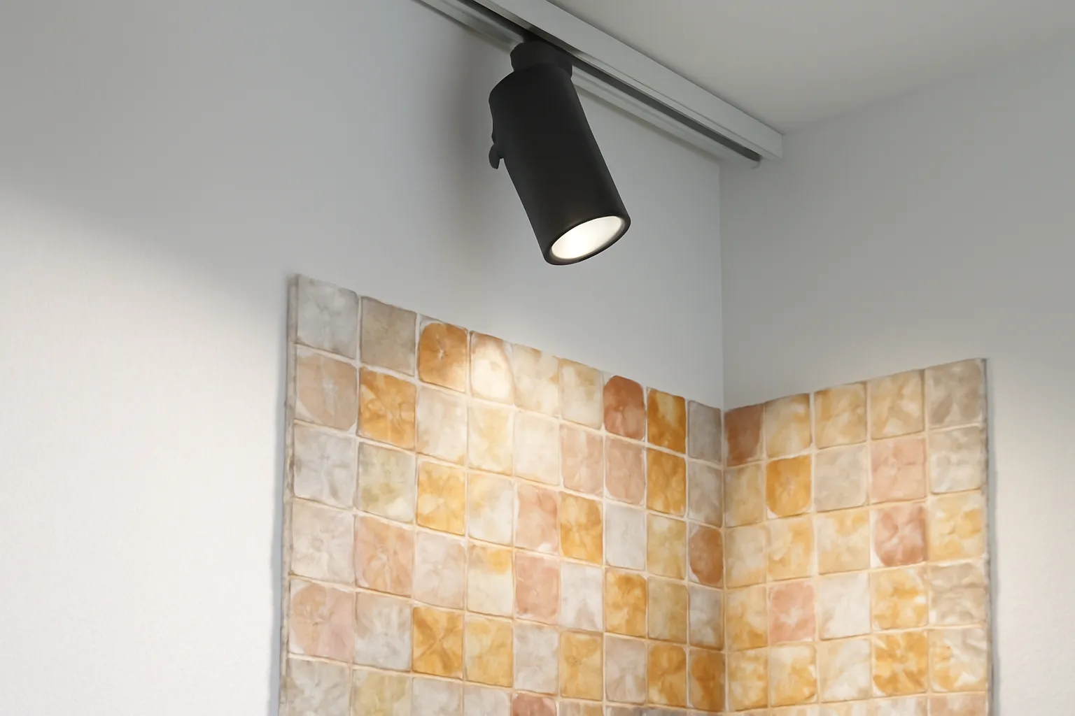 Đèn rọi ray trần chiếu xiên lên góc tranh đá thạch anh lấp lánh trên tường trắng